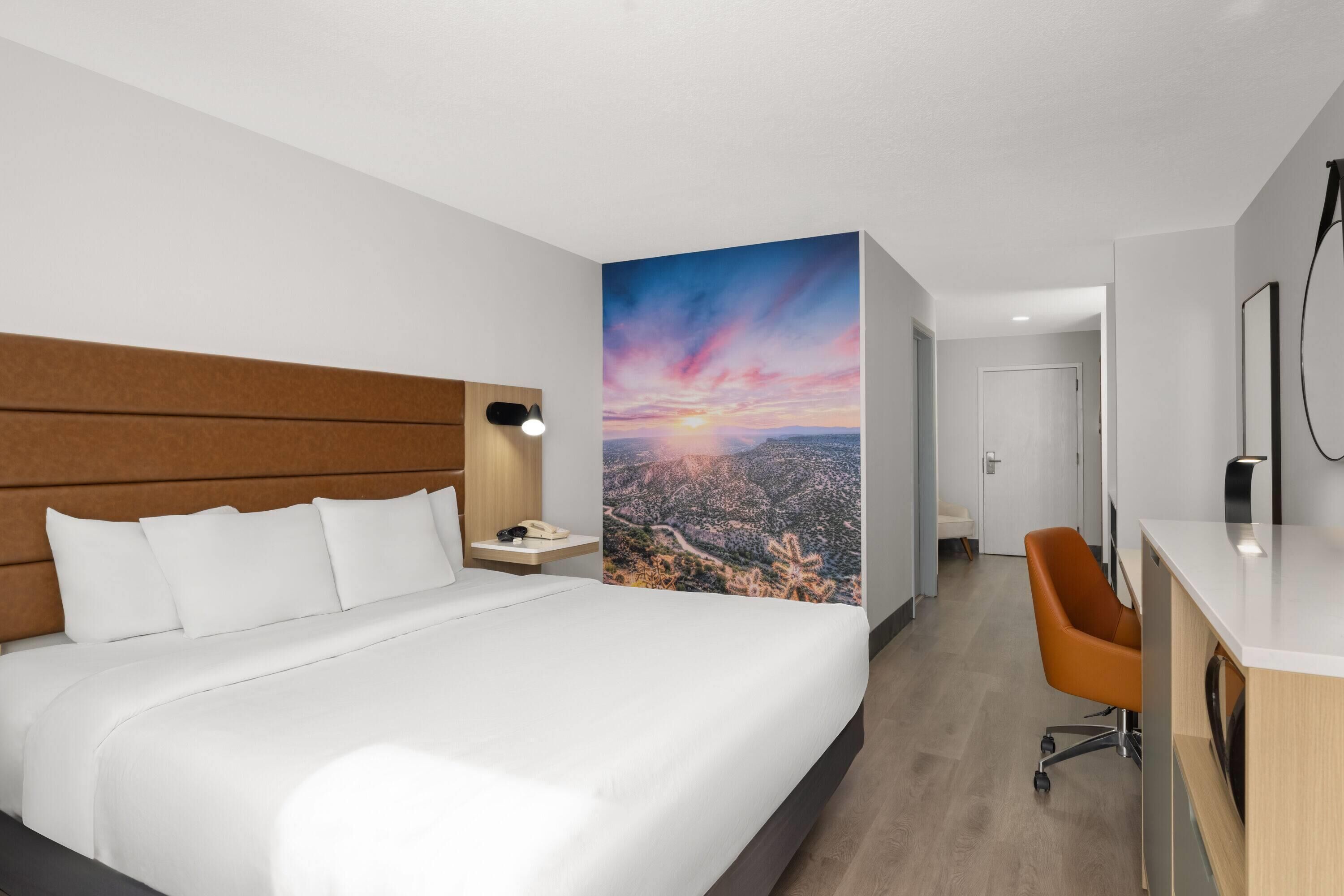 Moderni hotellihuone, jossa on suuri sänky, työpöytä ja seinällä kaupunkimaisemaa esittävä seinämaalaus.