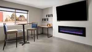Una habitación moderna con una televisión grande, una chimenea y una ventana que ofrece vistas a árboles y edificios.