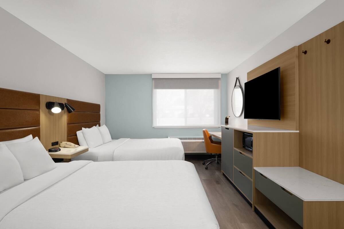 Una habitación de hotel con dos camas, un escritorio, una silla, un televisor y una ventana.