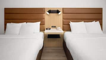 Quarto de hotel com duas camas, cabeceira de madeira, mesa de cabeceira com abajur e telefone.