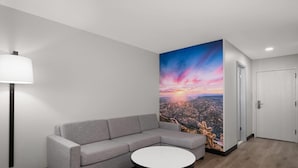 Una habitación moderna con un sofá gris, una mesa redonda blanca y un mural grande con un paisaje urbano en la pared.