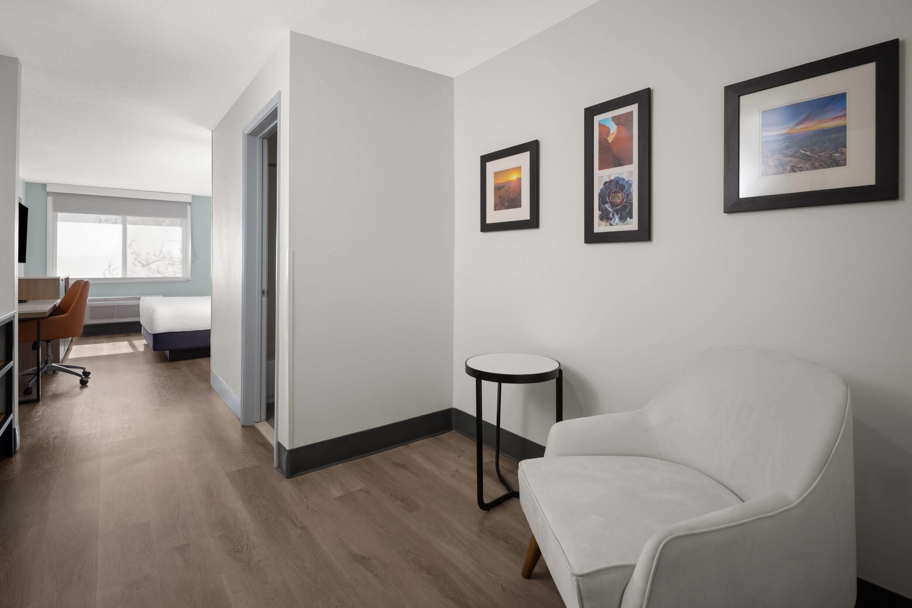 A modern hotel room with a bed, a desk, a chair, and a round table. There are three framed pictures on the wall.