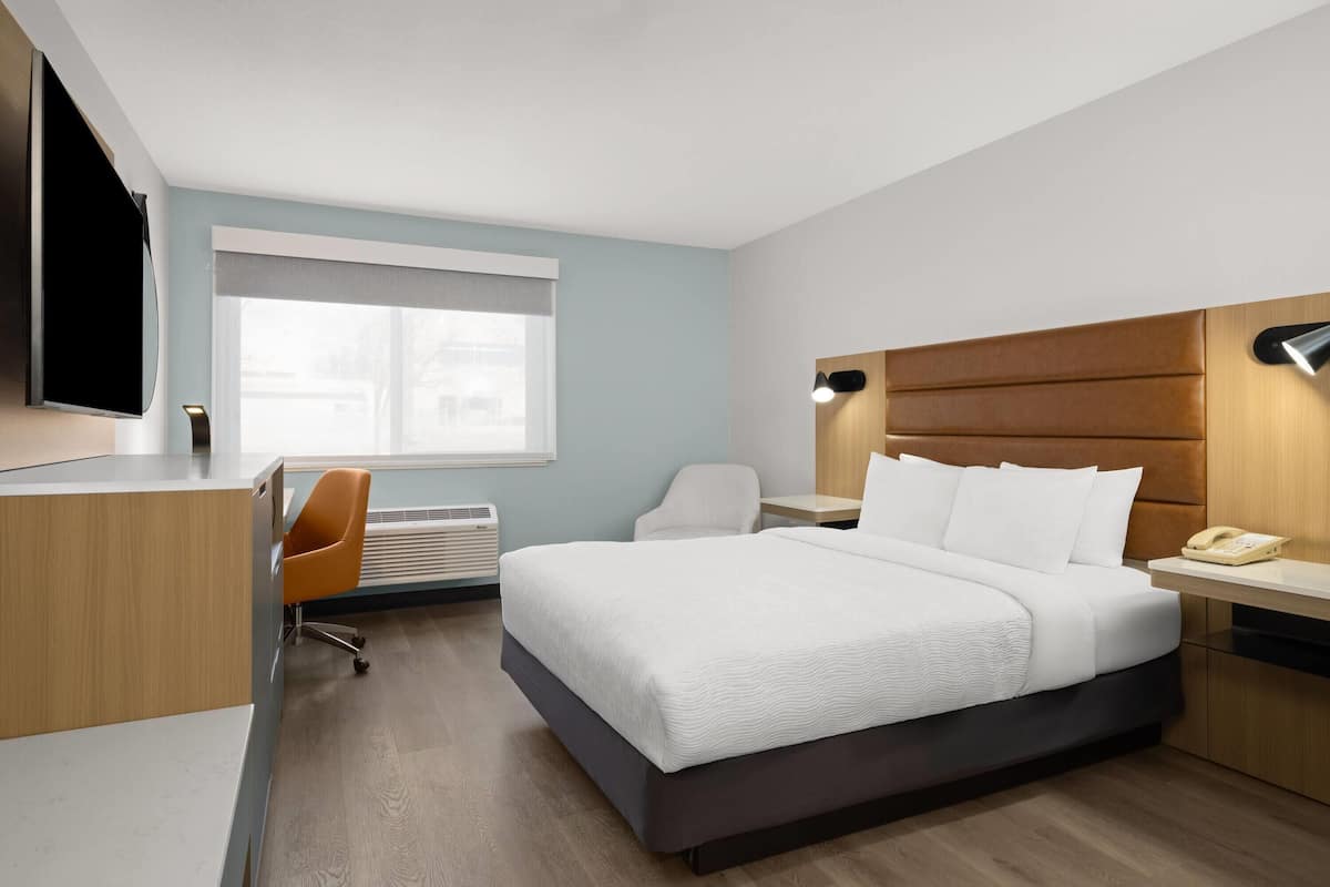 A hotel room with a bed, desk, chair, and a television.