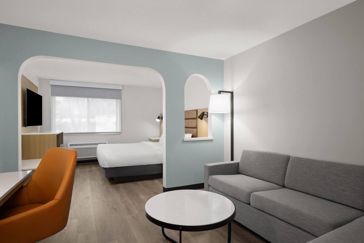 Una habitación de hotel moderna con una cama, un sofá, una mesa redonda y un televisor.