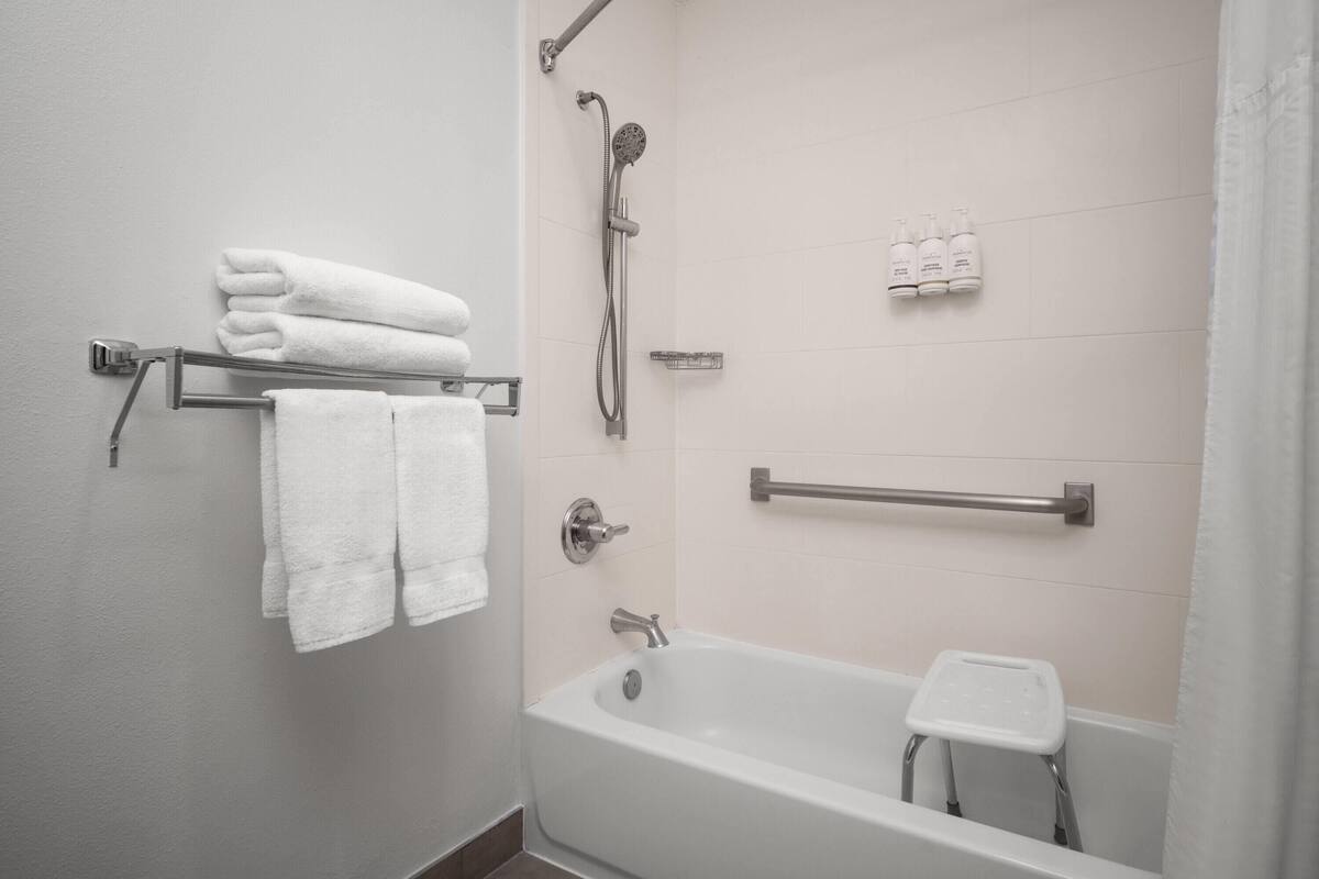 Un baño con una bañera, ducha, un perchero con toallas, un secamanos y un taburete pequeño.