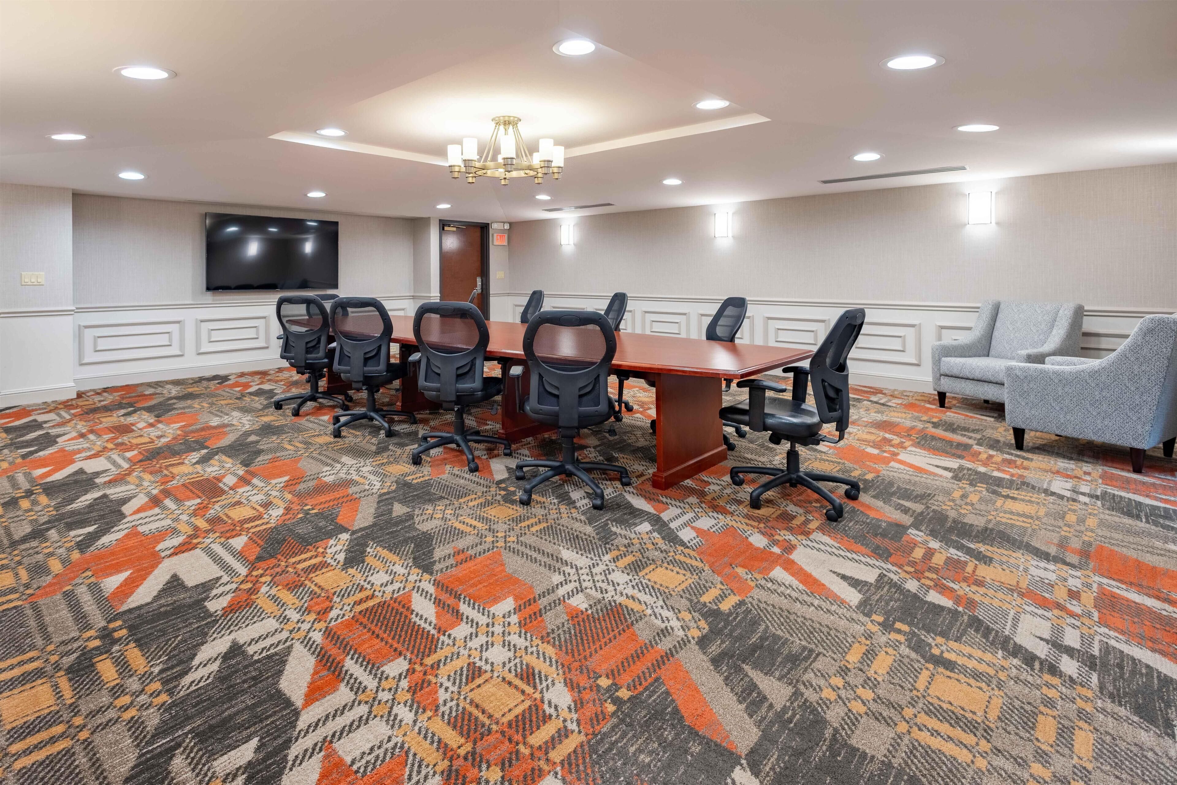 A conference room with a large table, six chairs, a television, and a patterned carpet.