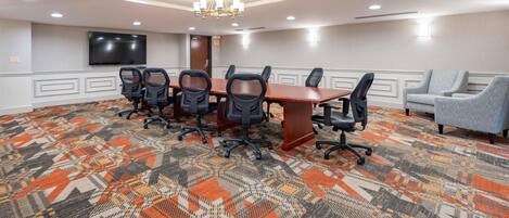 A conference room with a large table, six chairs, a television, and a patterned carpet.