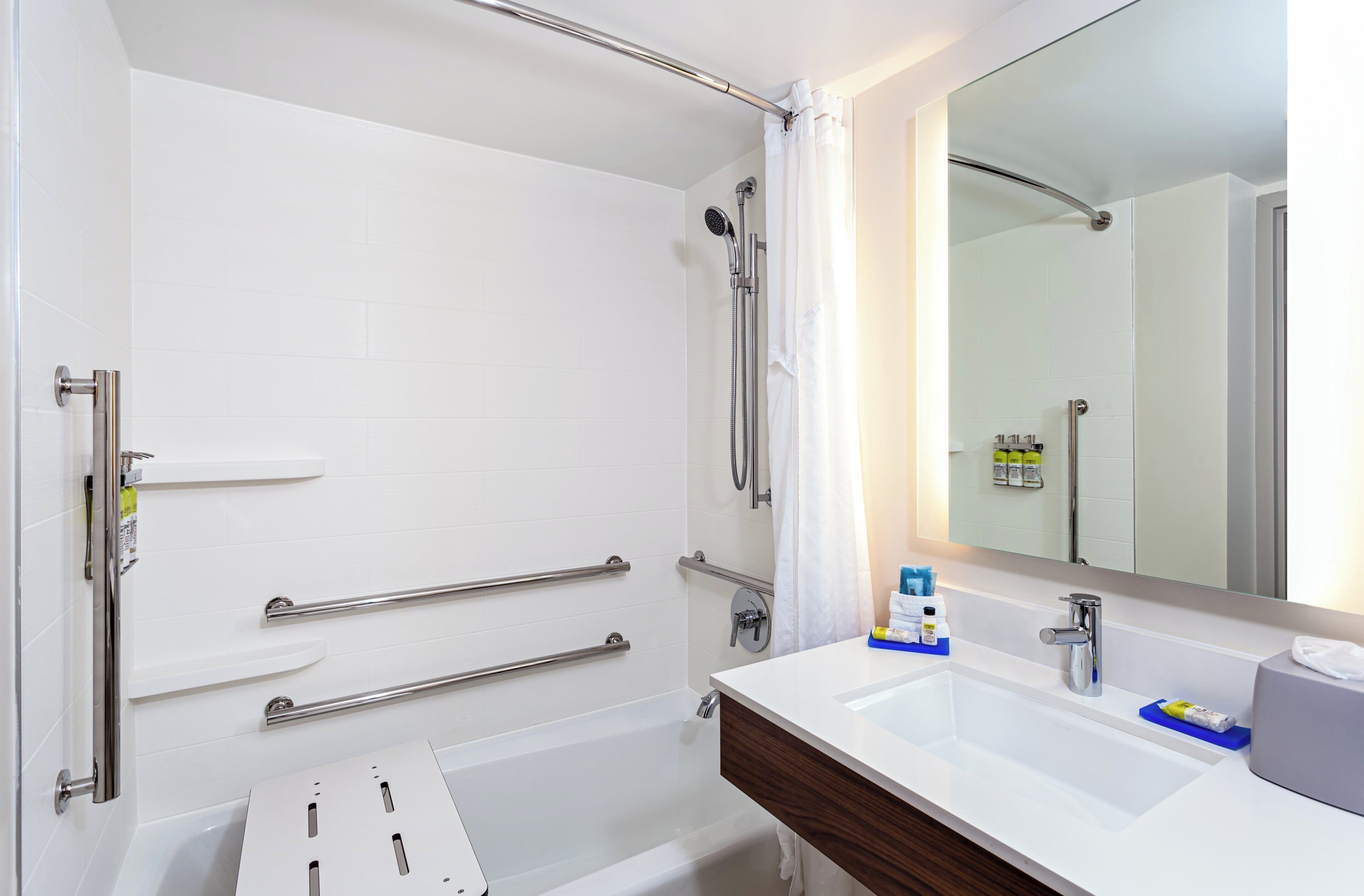A modern bathroom with a walk-in shower, grab bars, a white sink, and a large mirror.