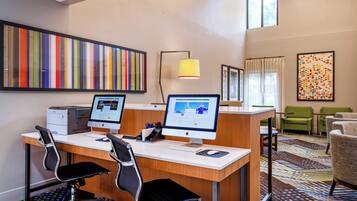 A hotel room with two desktop computers, a printer, a desk, two chairs, a lamp, and a large window.