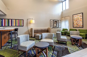 A hotel lobby with a sofa, chairs, a desk, and artwork on the walls. - Holiday Inn Express Tampa-Brandon by IHG (Brandon)