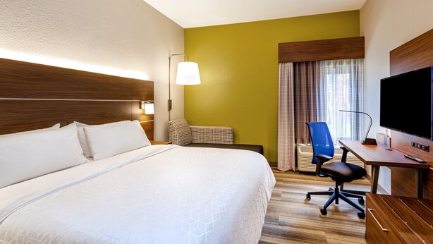 Une chambre d’hôtel avec un grand lit, un bureau avec une chaise, une télévision et une fenêtre avec des rideaux.