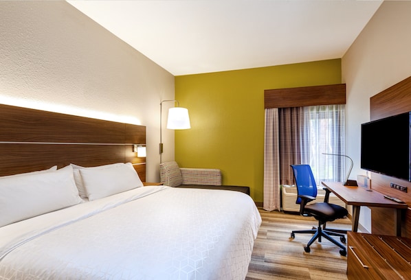 Habitación de hotel con una cama grande, un escritorio con una silla, un televisor y una ventana con cortinas.