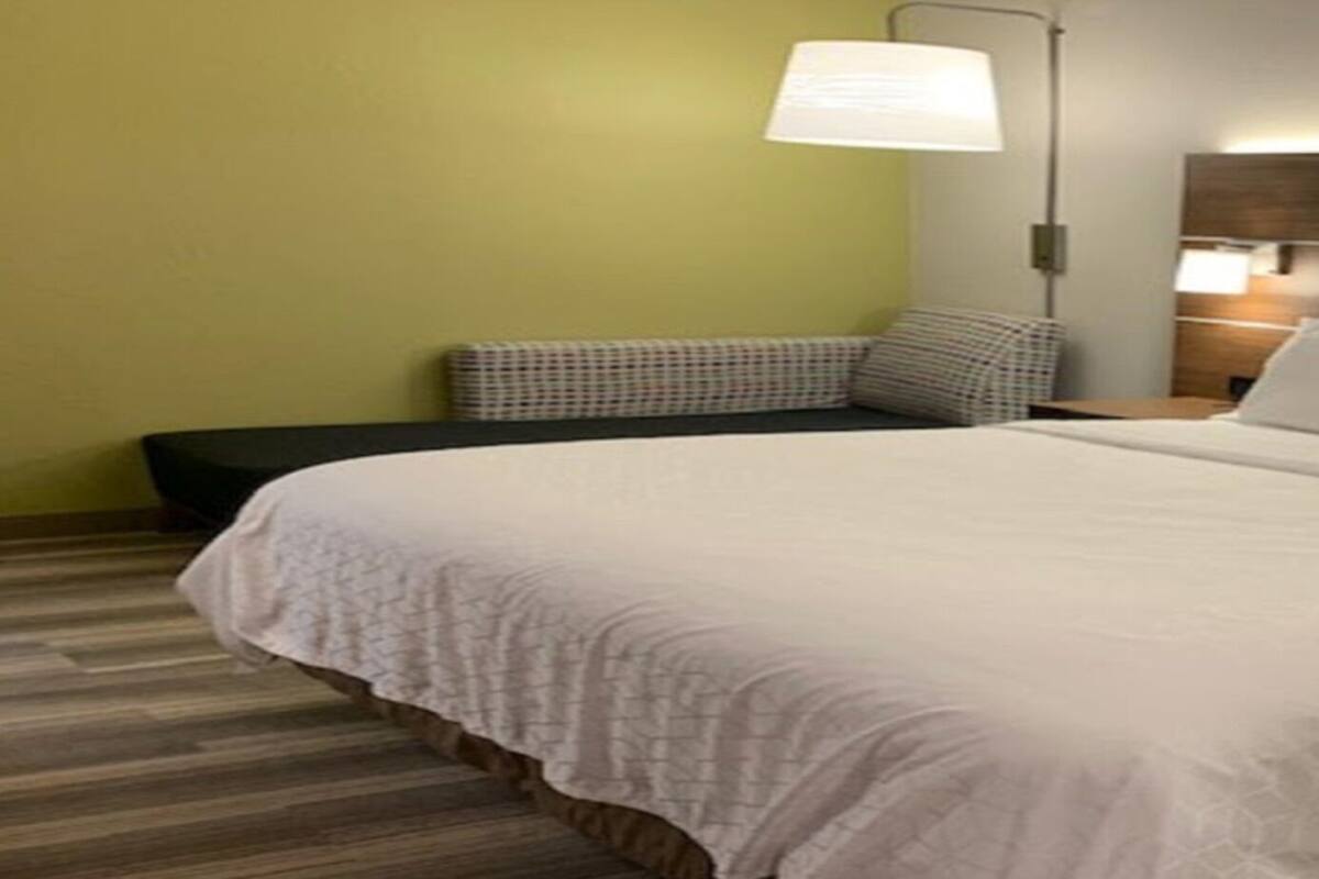 Ein Hotelzimmer mit einem großen Bett, einem Nachttisch mit Lampe sowie einer kleinen Sitzecke mit Bank und Kissen.