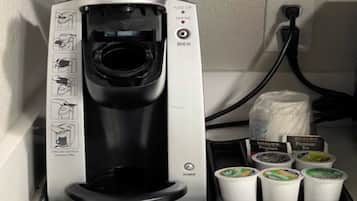 Une machine à café Keurig, avec quatre gobelets à café jetables et un sachet de dosettes de café.