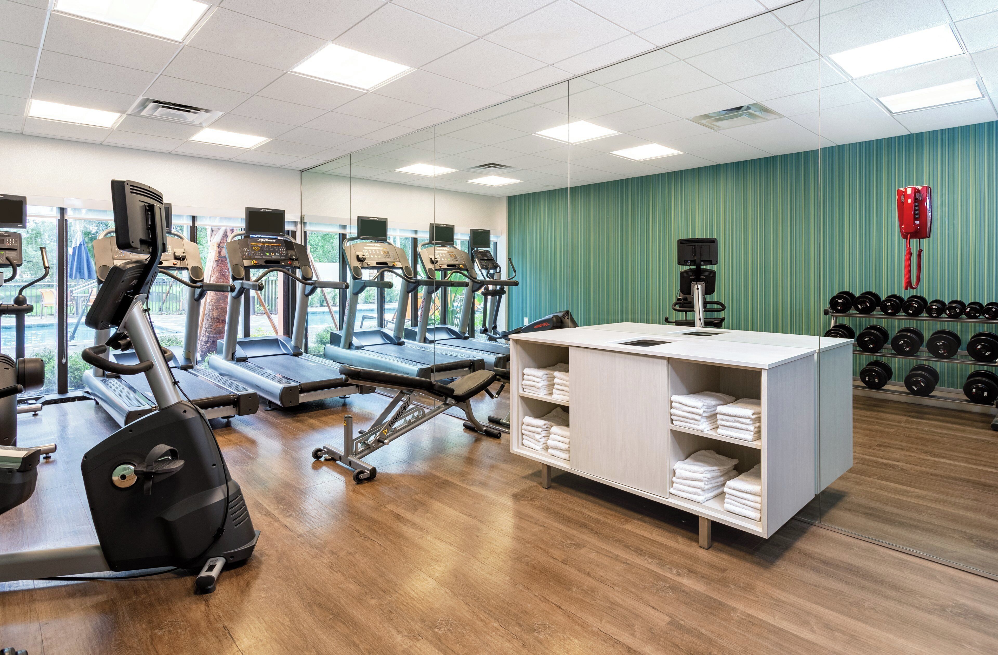 Un gimnasio con cintas de correr, elíptica, banco de pesas y un estante con mancuernas.