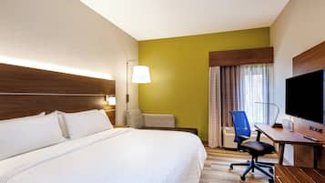 A hotel room with a large bed, a desk with a chair, a television, and a window with curtains.