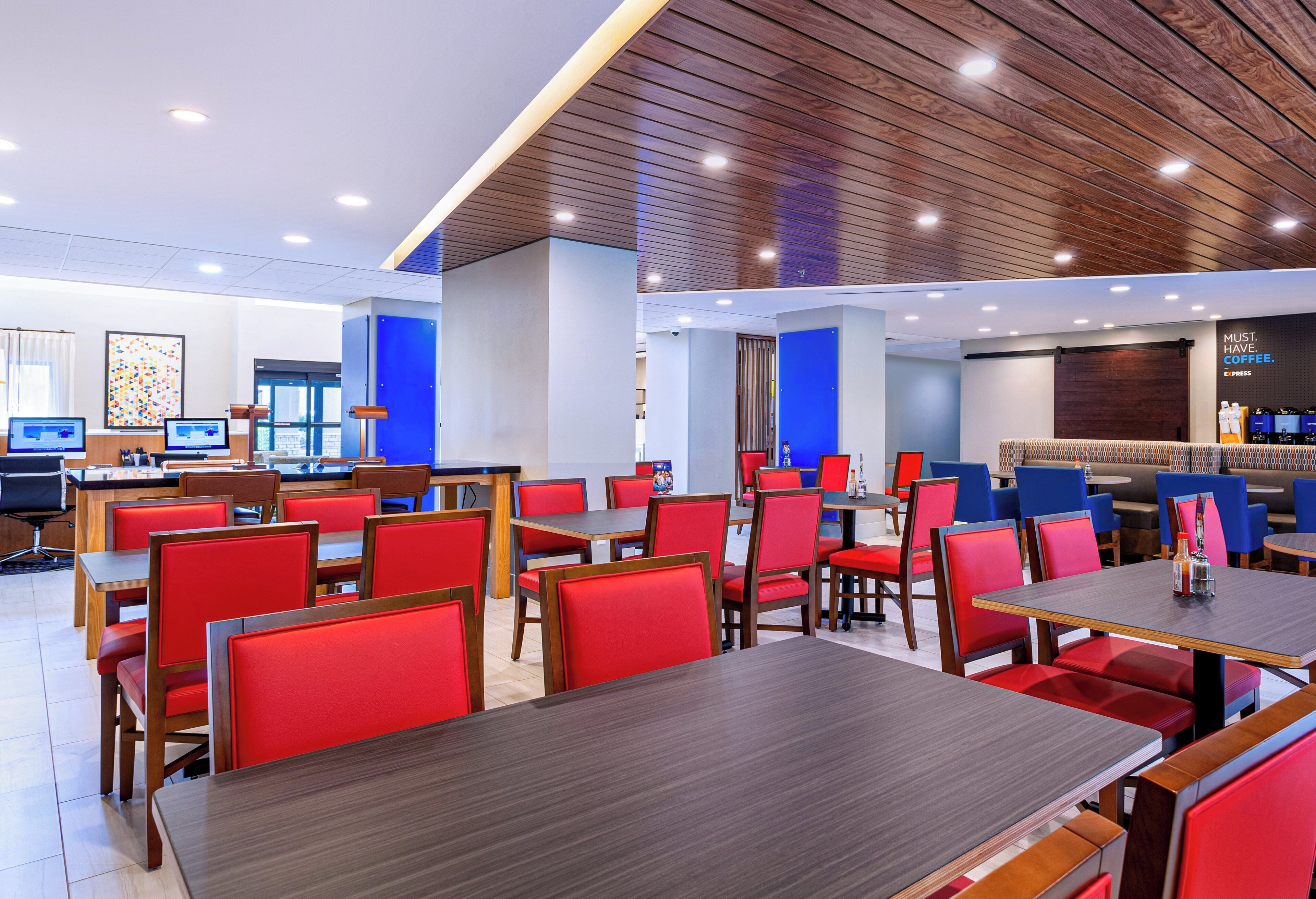 Interior de restaurante moderno com assentos estofados em vermelho, mesas de madeira e iluminação embutida no teto.