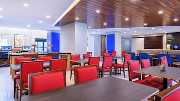Interior de restaurante moderno com assentos estofados em vermelho, mesas de madeira e iluminação embutida no teto.