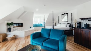 Un dormitorio moderno con una cama con dosel, un rincón de descanso con un sofá azul y una kitchenette con armarios de madera oscura.