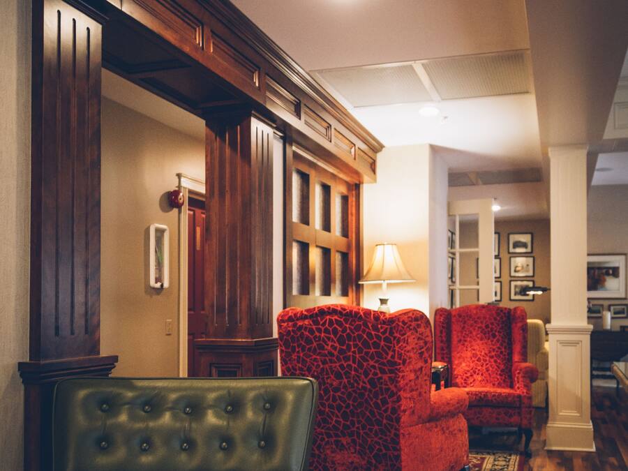 A hallway with wooden flooring, a green leather bench, and two red patterned armchairs.