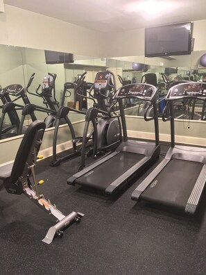 Uma academia com esteiras, bicicleta ergométrica e um banco de musculação.