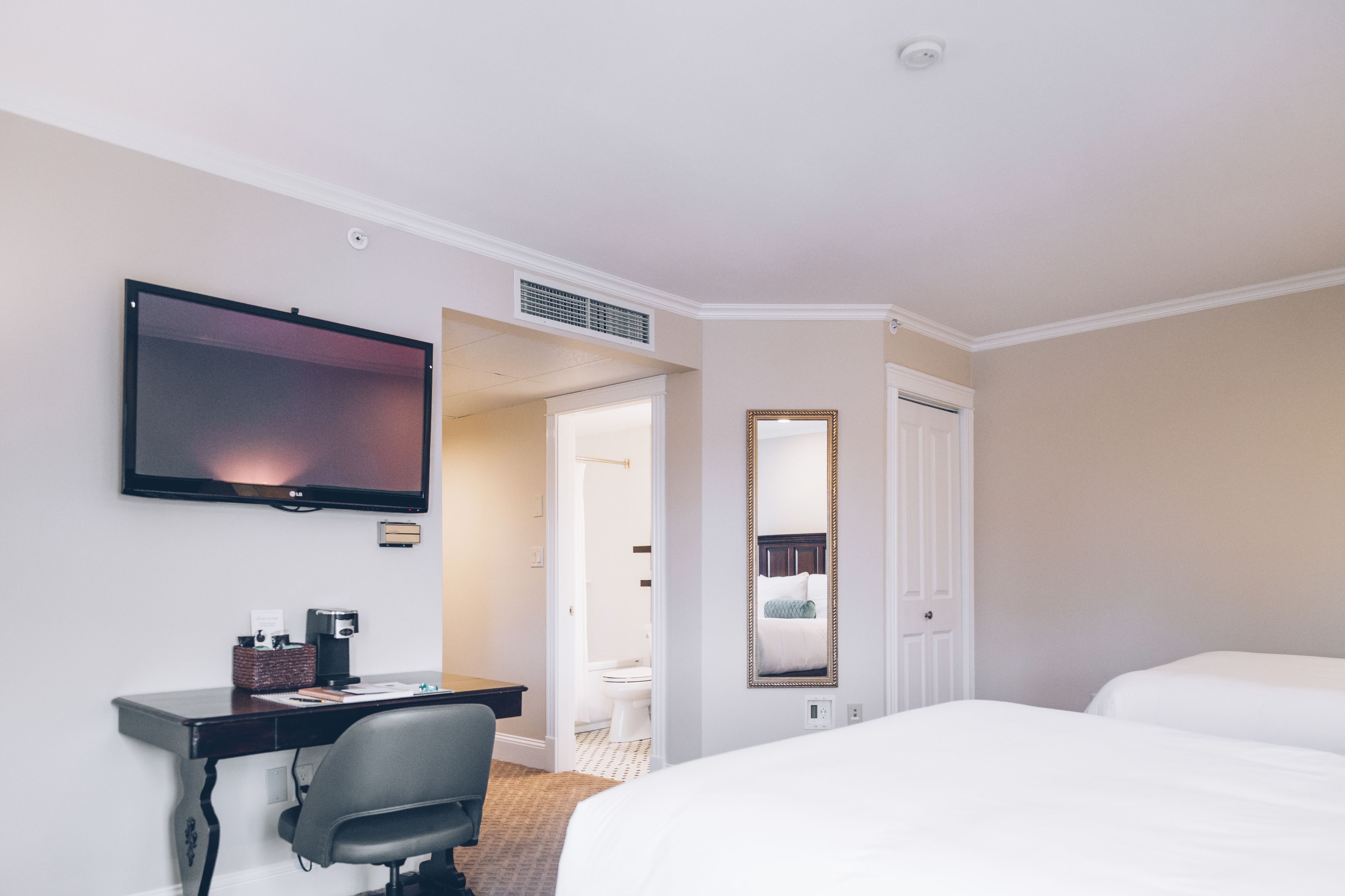 A hotel room with a bed, a desk with a chair, a television, a mirror, and a door leading to a bathroom.