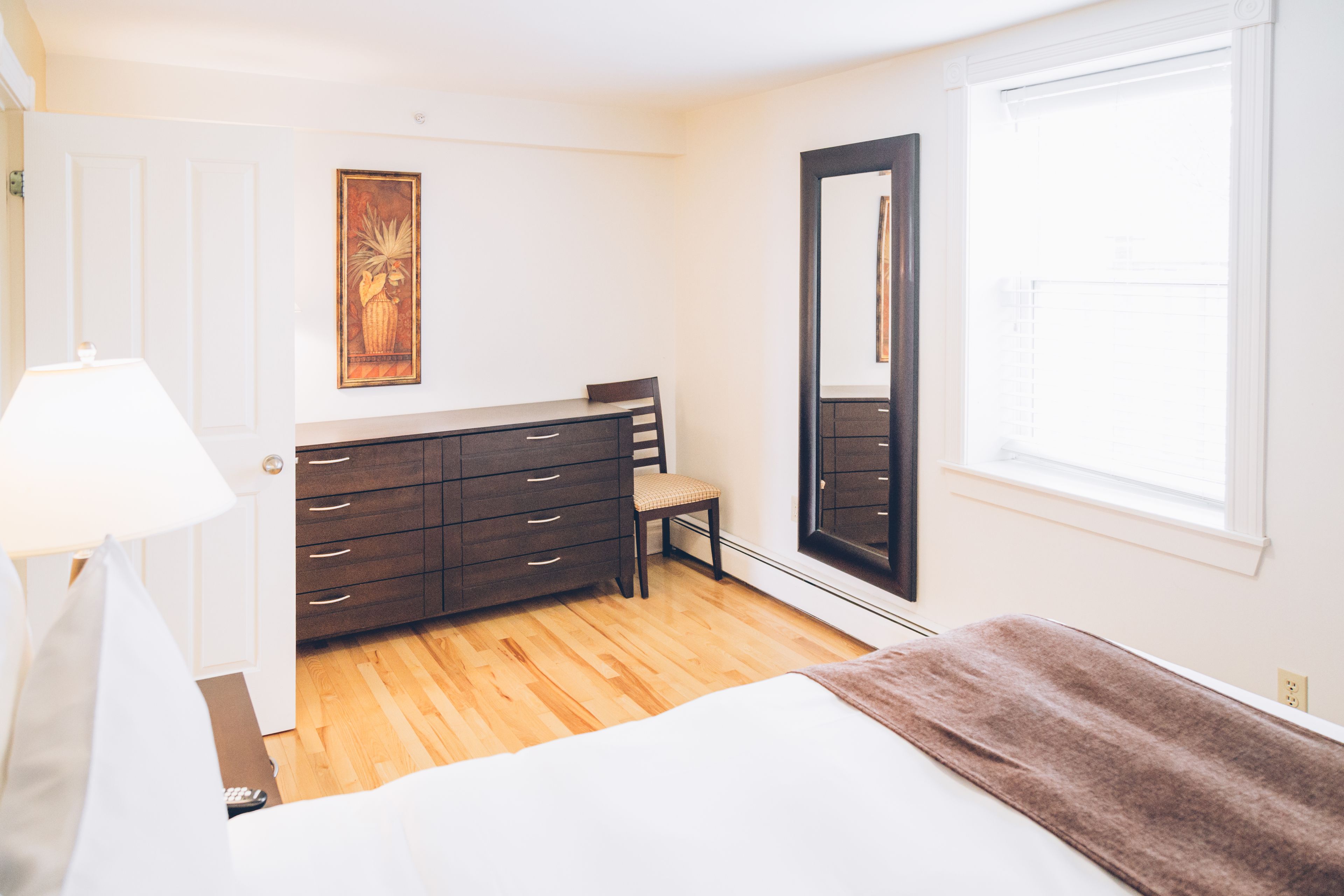 A bedroom with a bed, a dresser, a chair, a mirror, and a window.