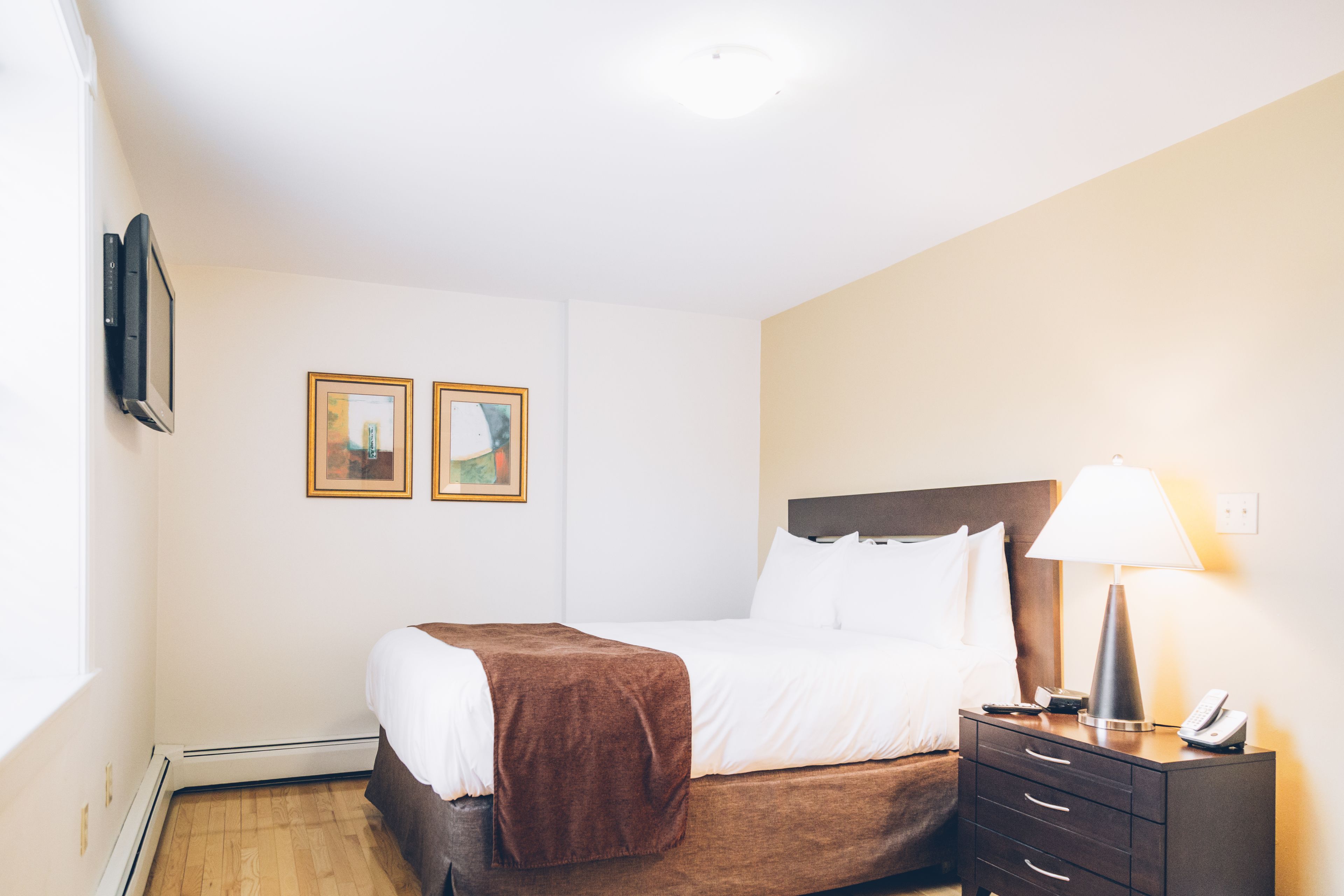 A hotel room with a bed, bedside table, lamp, and two framed pictures on the wall.