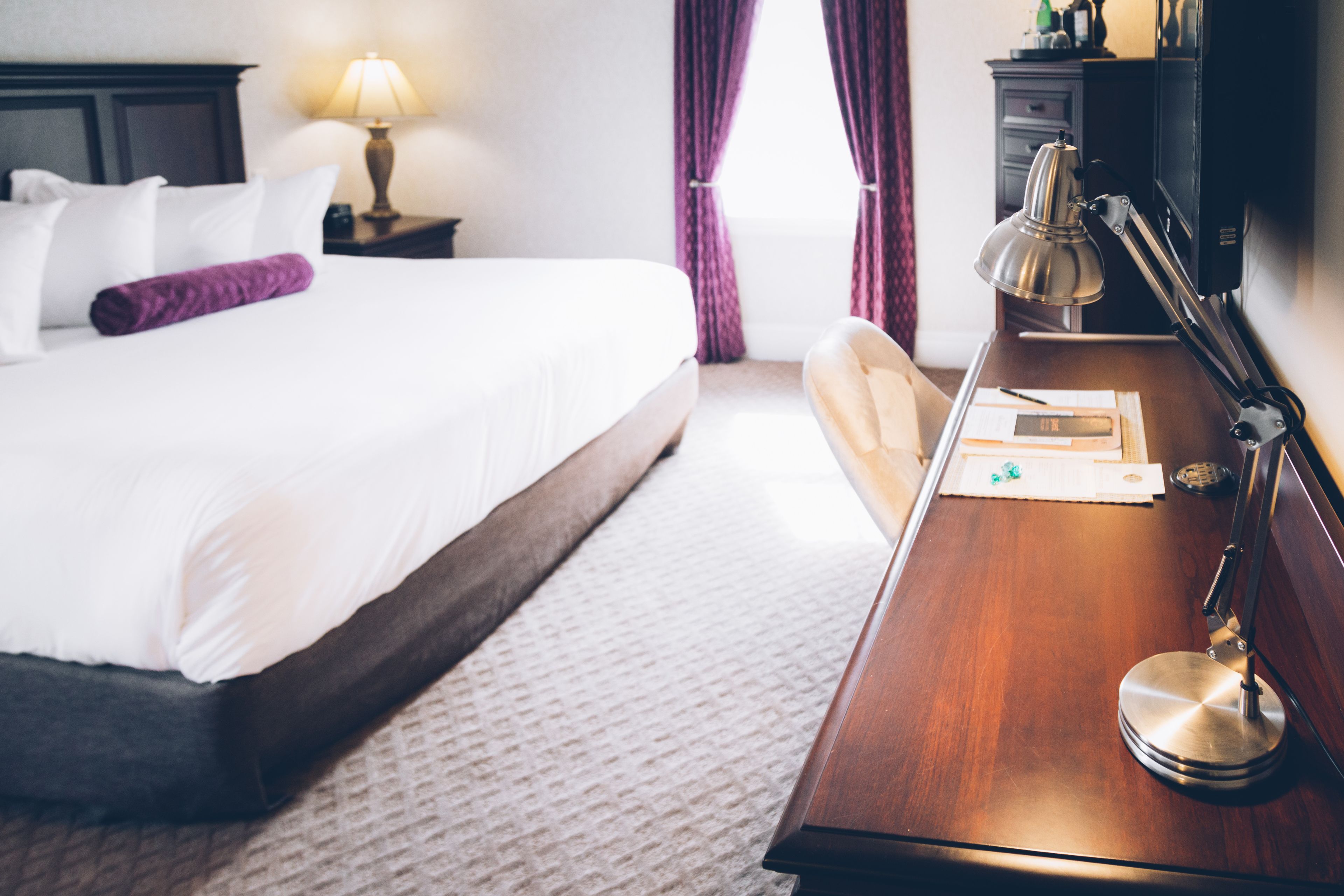 Une chambre d’hôtel avec un lit bien fait, un bureau en bois avec une lampe et une table de chevet avec une lampe.