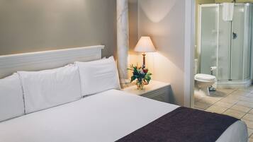 A hotel room with a large bed, a nightstand with a lamp, a bathroom with a shower, and a toilet.