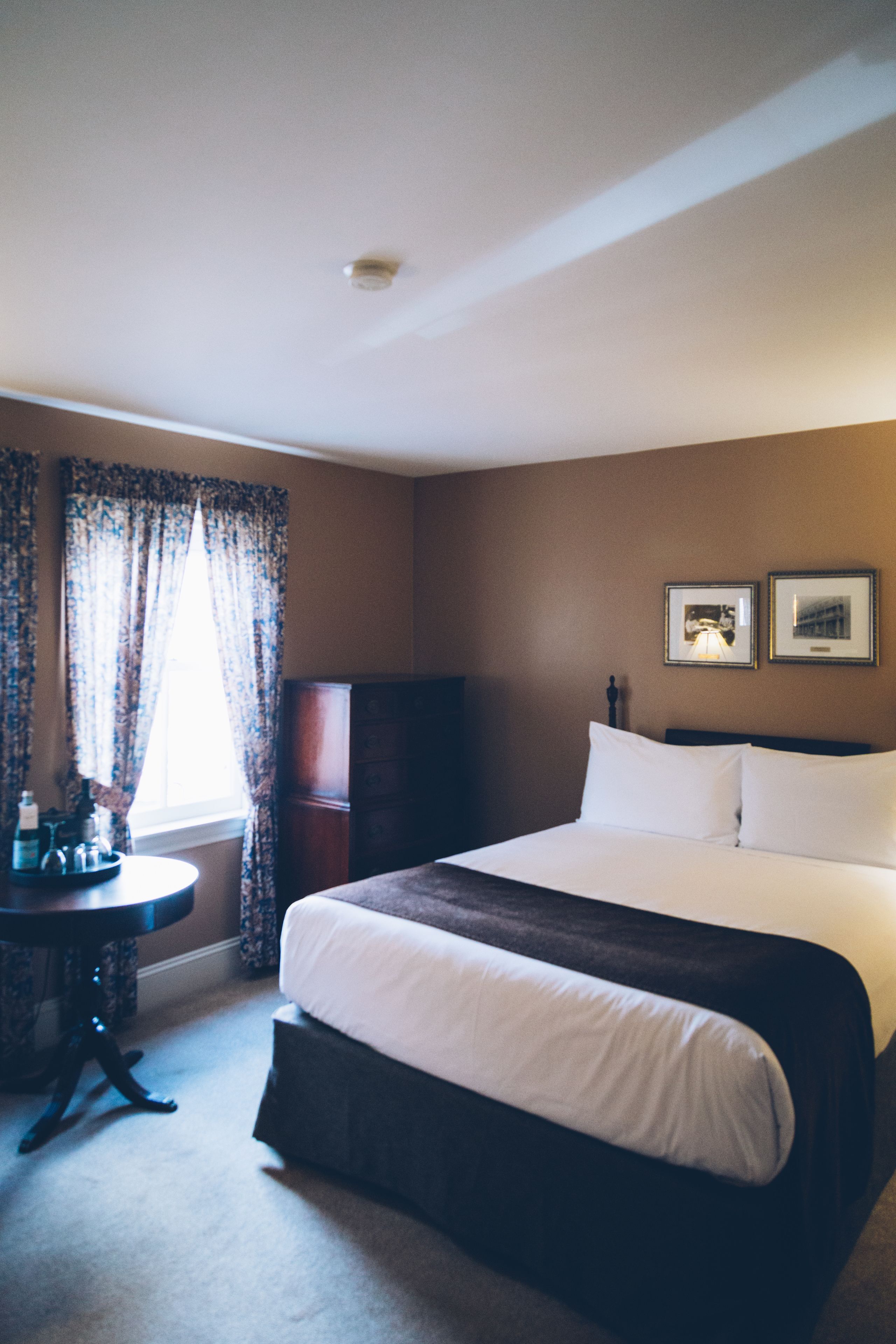 A hotel room with a large bed, a nightstand, a dresser, and a window with curtains.