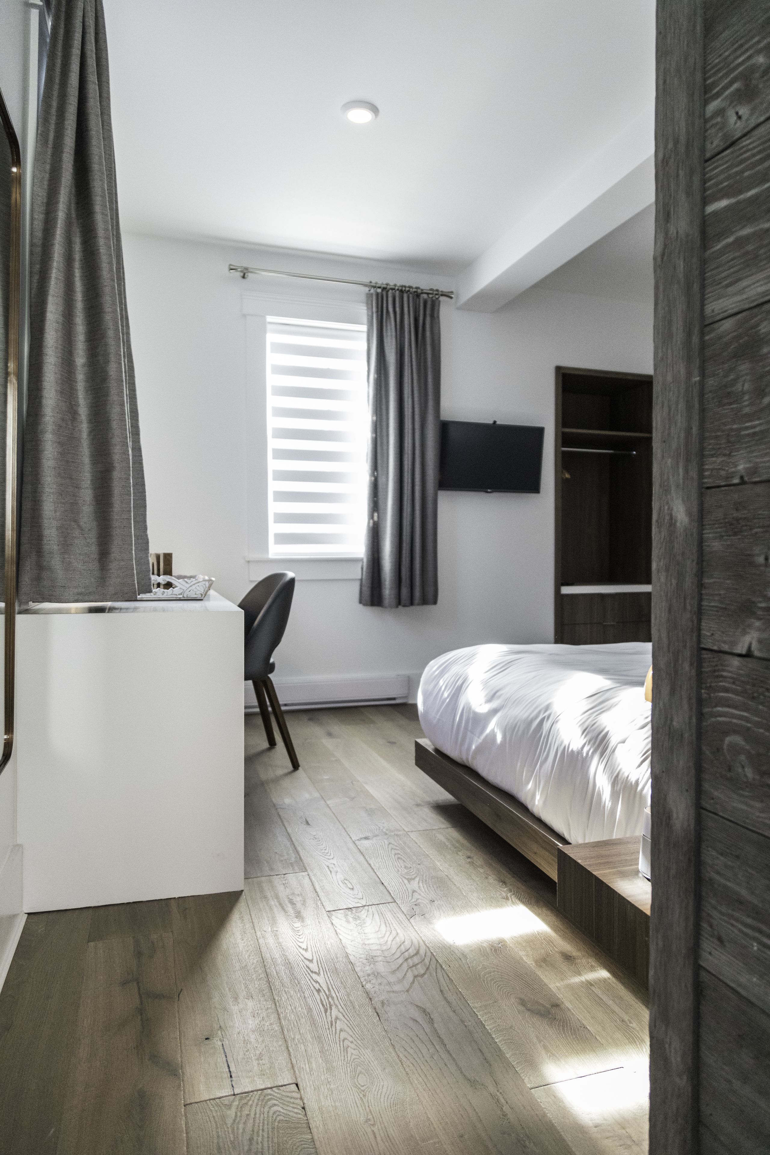 Une chambre moderne avec un plancher en bois, un lit, un bureau et un téléviseur fixé au mur.