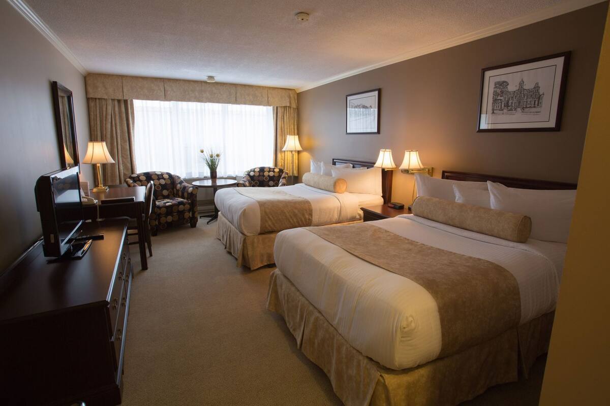 A hotel room with two beds, a desk with a TV, a chair, and lamps.