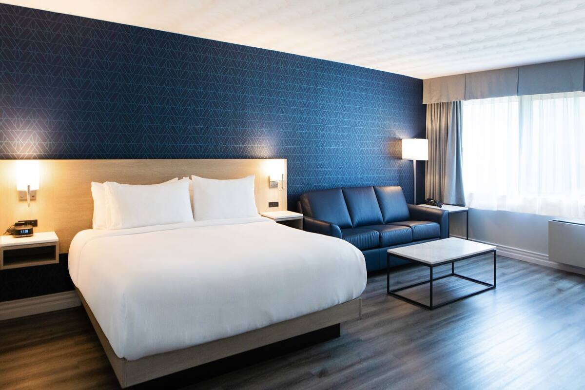 A hotel room with a bed, a sofa, a coffee table, and a nightstand with a lamp.