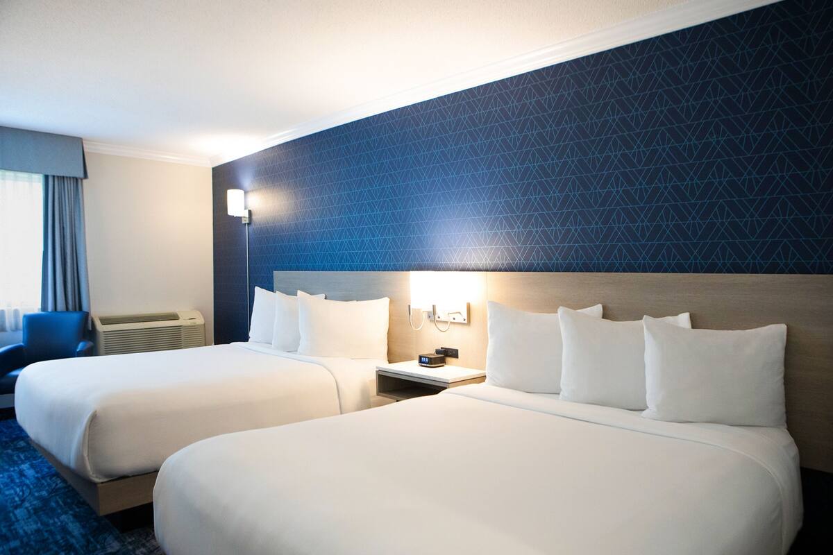 A hotel room with two beds, a nightstand, a lamp, and a blue carpet.
