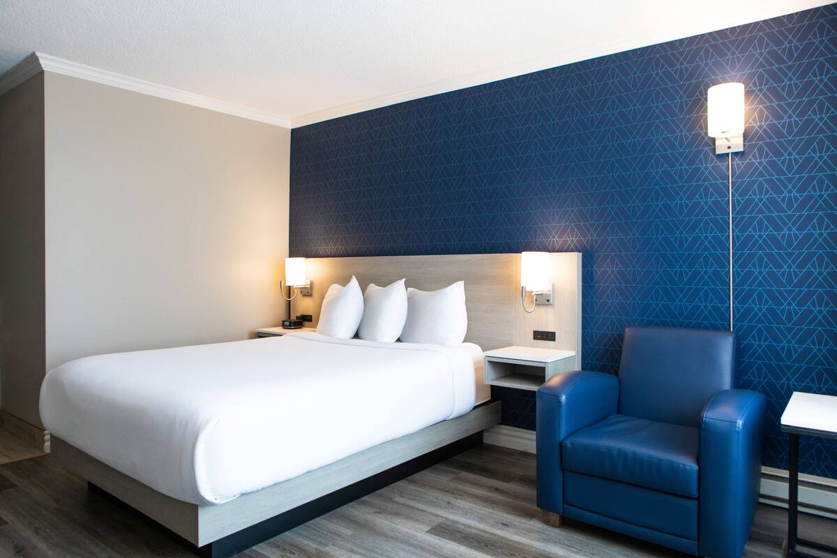 A hotel room with a bed, a chair, a nightstand, and a wall with a geometric pattern.