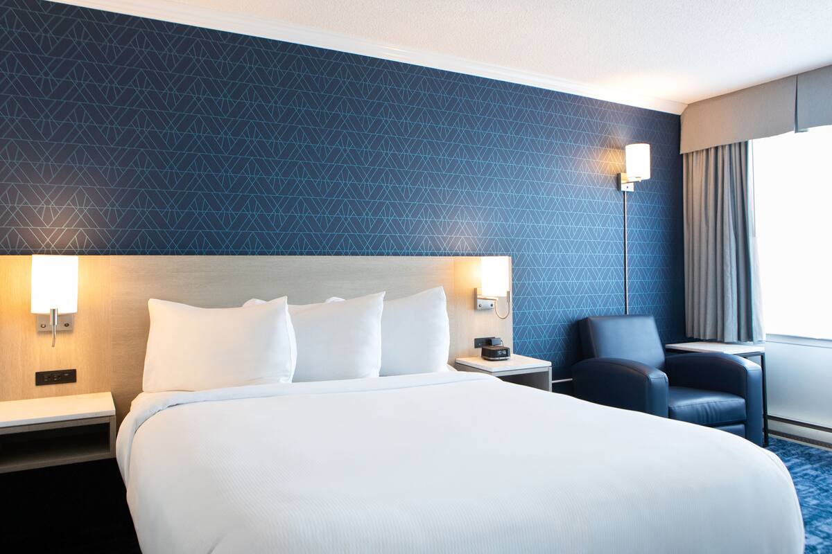A hotel room with a large bed, bedside tables, a desk, a chair, and a lamp.