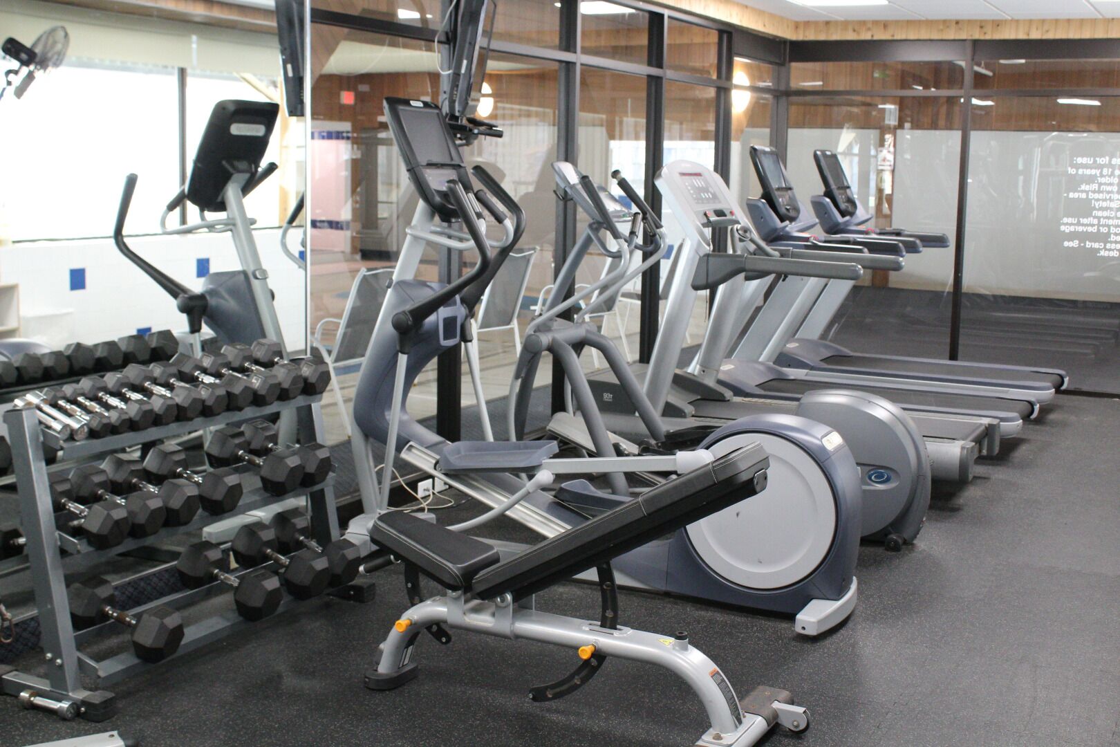 A gym with various exercise machines, dumbbells, and treadmills.