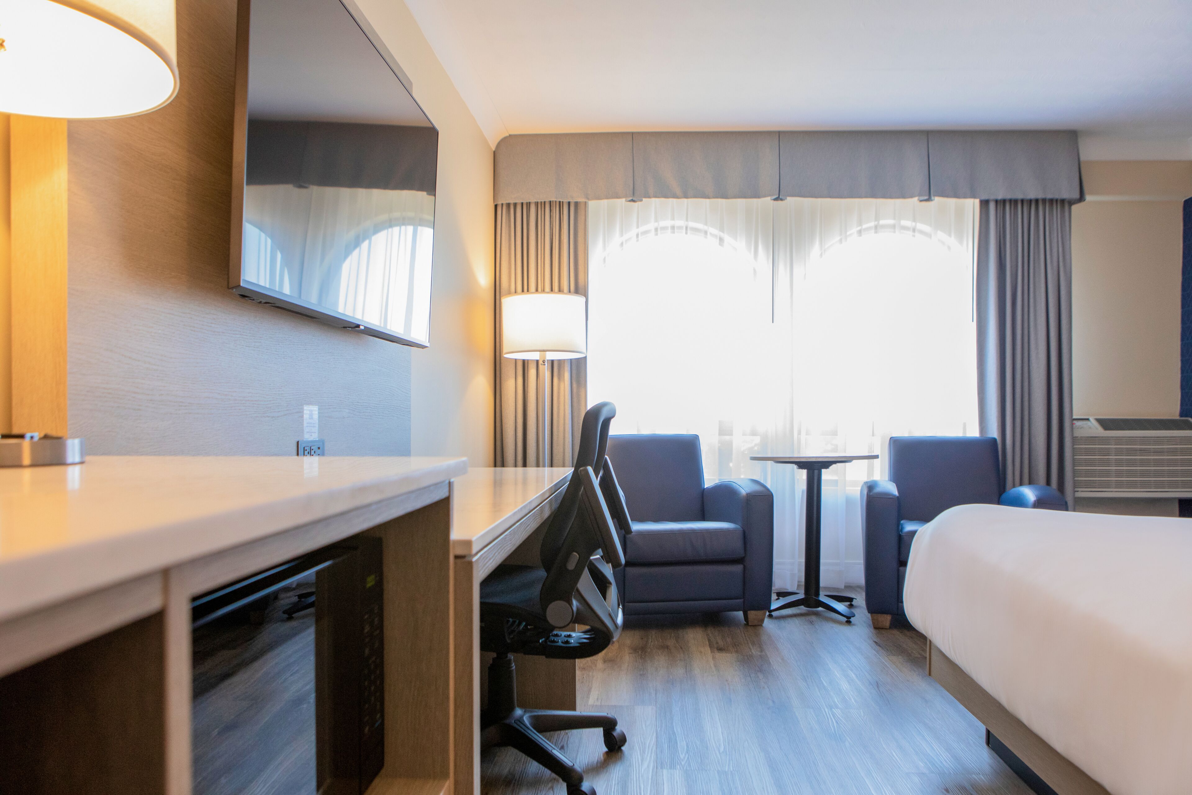 Una habitación de hotel con cama, escritorio, sillas, una mesita y televisor.