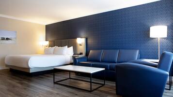 A hotel room with a bed, a sofa, a coffee table, a lamp, and a wall with a geometric pattern.