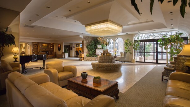 A spacious lobby with leather sofas, a grand piano, a large chandelier, and a potted plant arrangement.