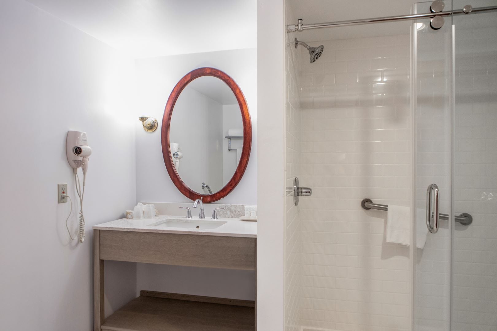 A bathroom with a sink, mirror, hairdryer, and shower.