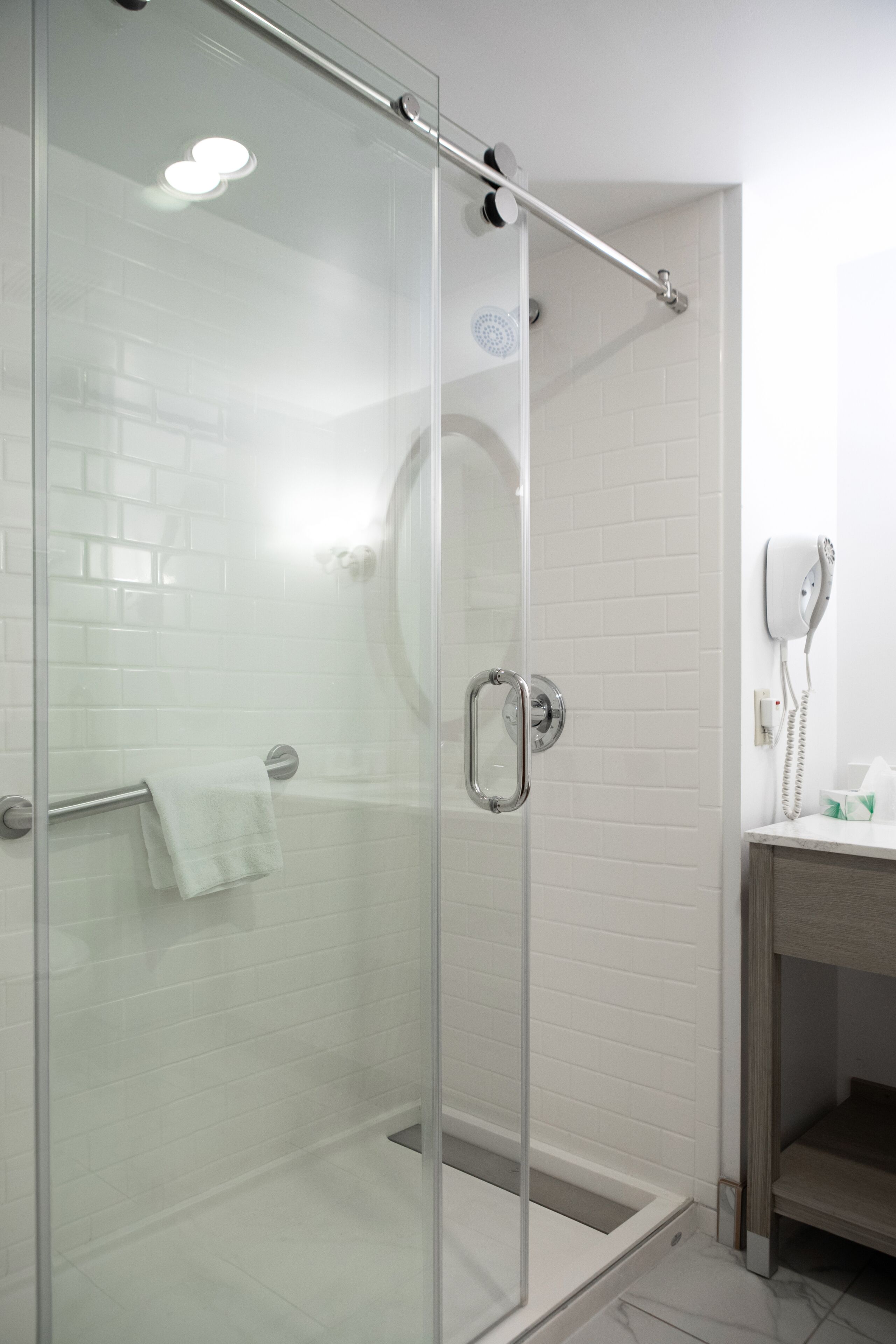A glass-enclosed shower with a towel rack, a handheld showerhead, and a wall-mounted telephone.