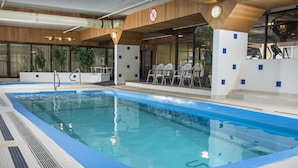 An indoor swimming pool with clear blue water, a no swimming sign, and a seating area with chairs and tables.
