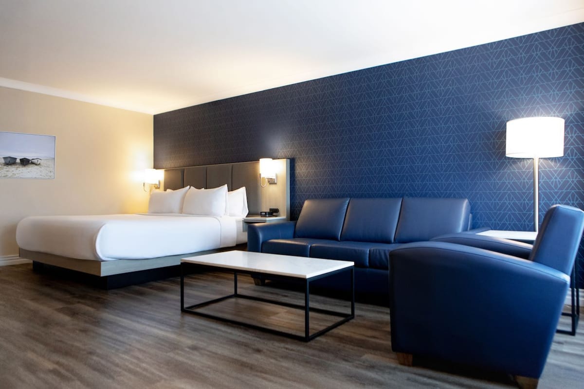 A hotel room with a bed, a sofa, a coffee table, and a lamp.