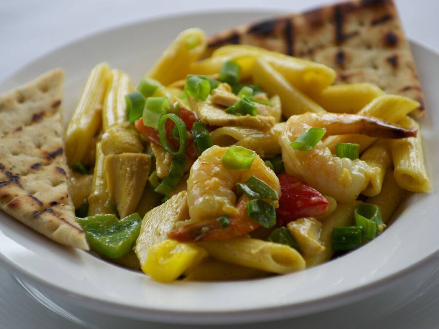 Een bord pasta met garnalen, groenten en een stuk platbrood.