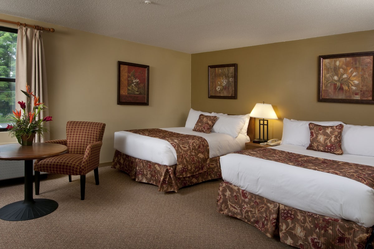 A hotel room with two beds, a chair, a table, and a lamp.