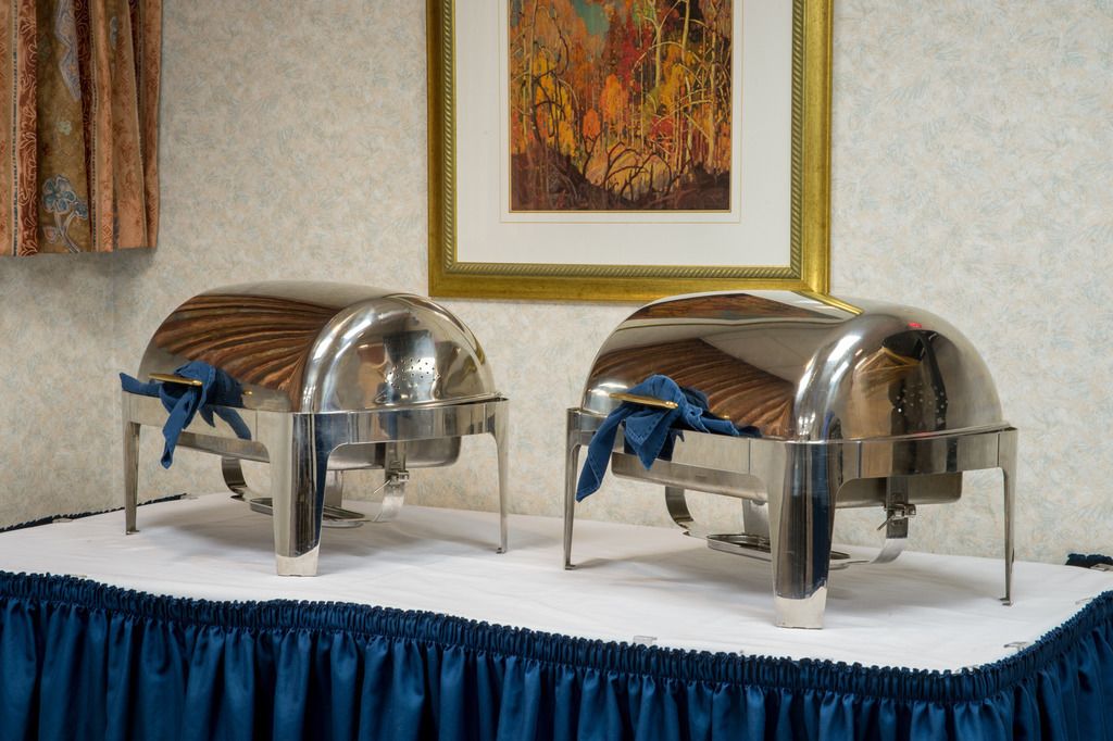 Duas unidades metálicas para serviço de alimentos sobre uma mesa branca com um pano azul.