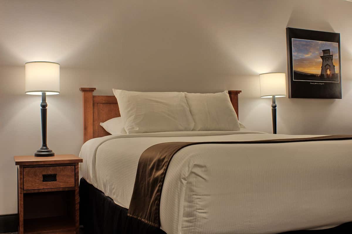 A neatly made bed with two bedside lamps, a wooden nightstand with a drawer, and a framed picture on the wall.