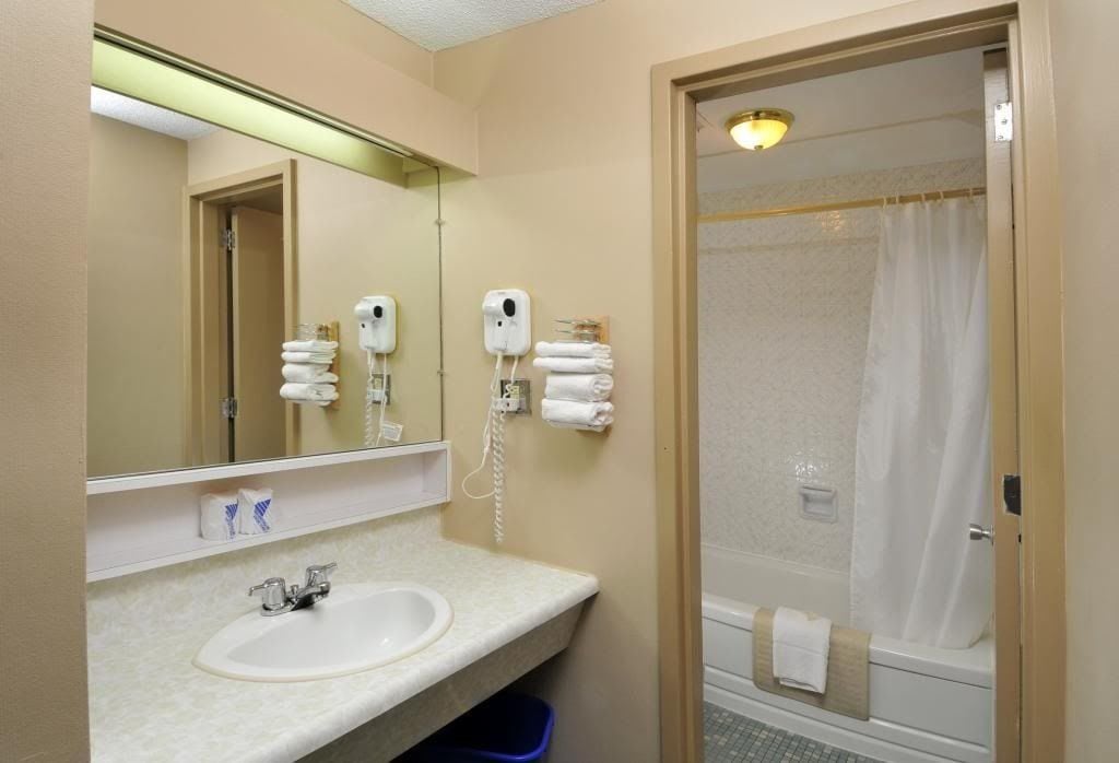 Baño de hotel con lavamanos, espejo, secador de pelo y ducha.